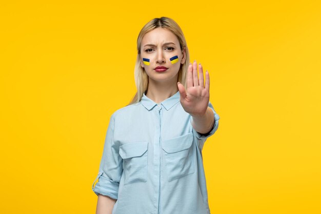 Russian ukrainian conflict cute girl yellow background with ukrainian flag on cheeks showing stop