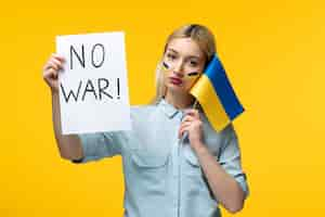 Free photo russian ukrainian conflict young cute girl with ukrainian flag on cheeks with flag and sign no war