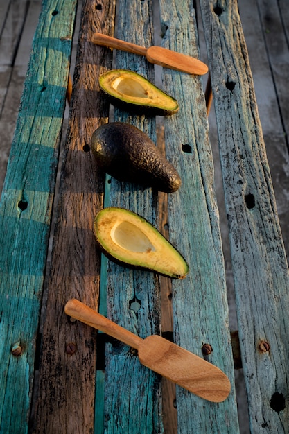 Rustic wooden surface with cut and whole avocados and wooden spoons