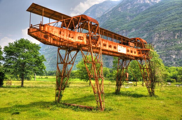 Rusty gantry crane in the green field with mountains