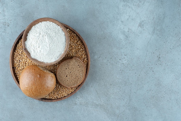 Rye bun with bowl of flour on wooden plate.