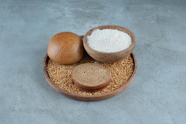 Rye bun with bowl of flour on wooden plate.