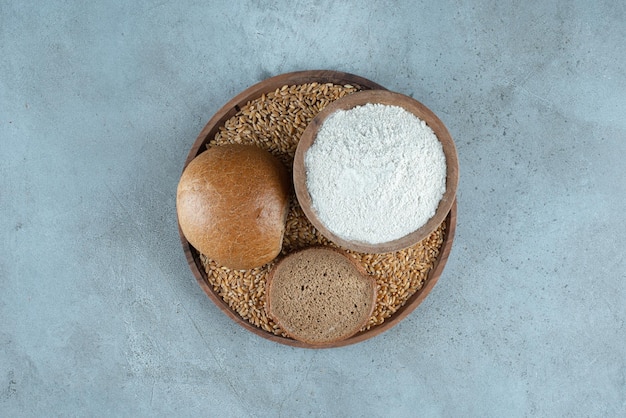 Rye bun with bowl of flour on wooden plate.