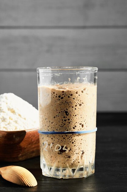 Rye and wheat sourdough starter in glass jar with ingredient flour Close up selective focus in the glass vertical frame