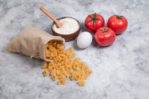 Sacco di maccheroni secchi a forma di conchiglia con una ciotola di legno di farina