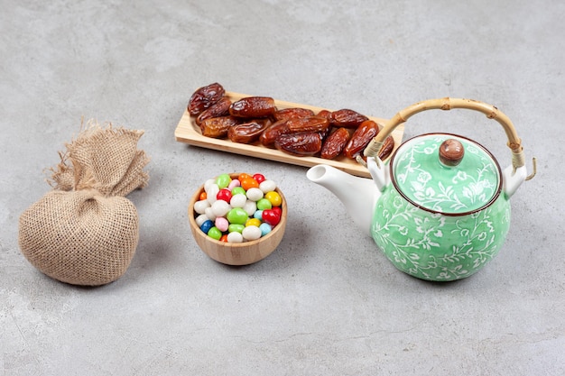 A sack, a bowl of candy, a wooden tray of dates and a teapot on marble surface.