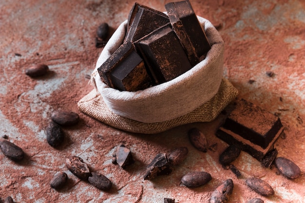 Sack of chocolate bar pieces and cocoa powder and beans on table