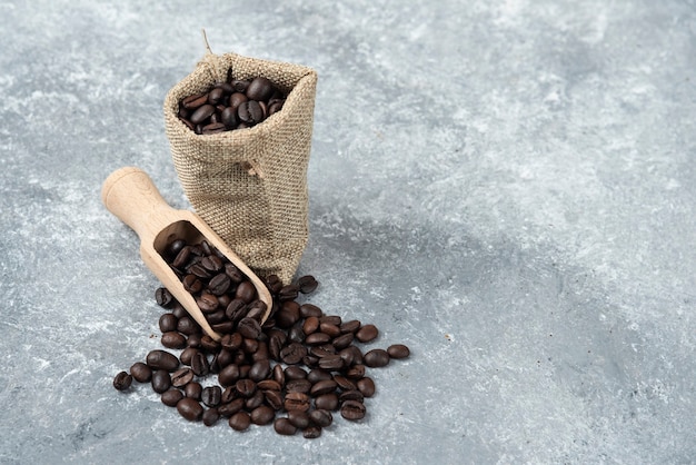 Sackcloth full of roasted coffee beans and wooden spoon on marble surface.