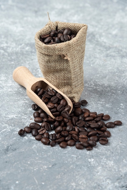 Sackcloth full of roasted coffee beans and wooden spoon on marble surface.