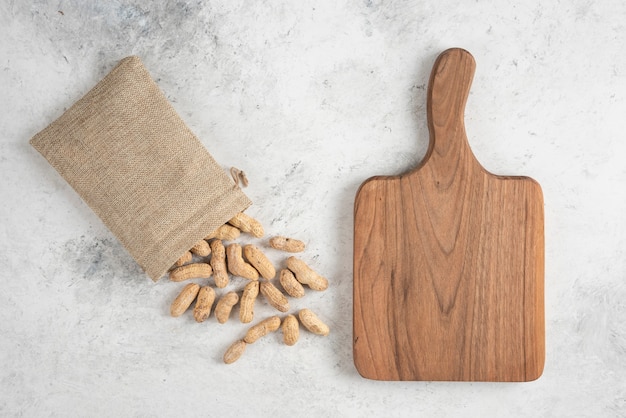 Sackcloth of organic roasted peanuts and wooden board on marble table. 