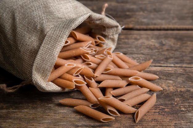 Sackcloth of raw penne pasta placed on wooden surface. High quality photo