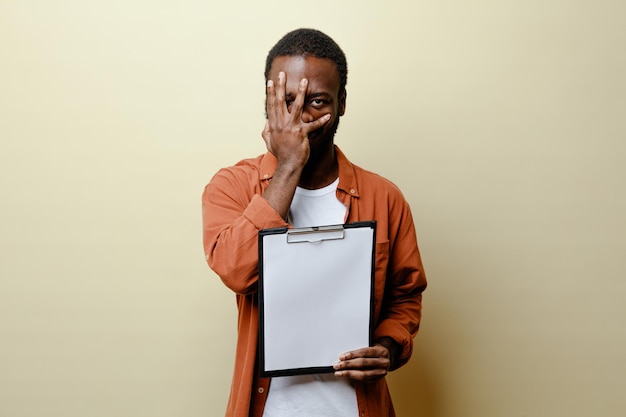 Sacred covered face with hand young african american male holding clipboard isolated on white background