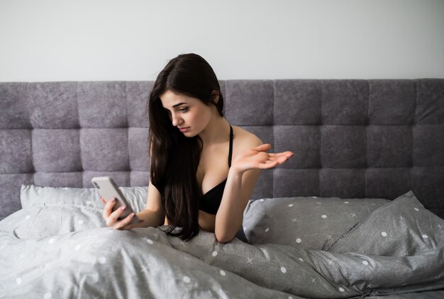 Sad asking woman reading message on the phone in the bed