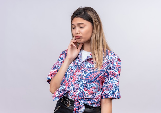 Foto gratuita una bella giovane donna triste che indossa la camicia stampata paisley che tiene la mano sulla faccia che ha dolore su una parete bianca