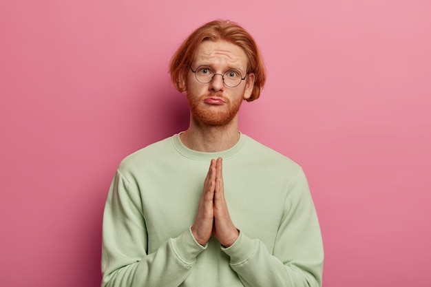 Free photo sad beseeching man with ginger hair and beard presses palms together