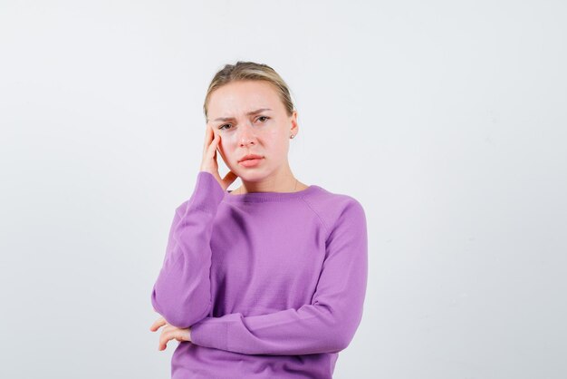 The sad blonde woman is holding her hand on temple on white background