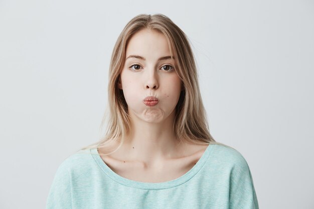 Sad blonde young woman has grumpy expression pouts her lips