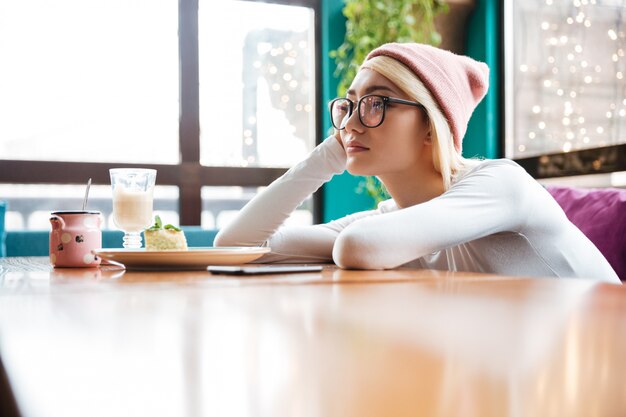 Sad bored young woman sitting at the table in cafe