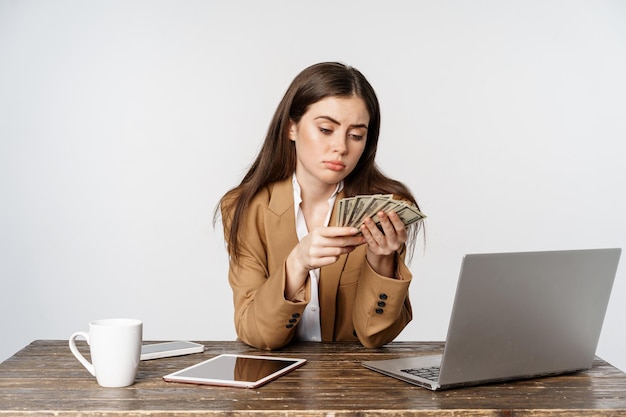 Foto gratuita donna d'affari triste che conta i soldi in ufficio con la faccia delusa sconvolta a basso reddito che posa contro chi...