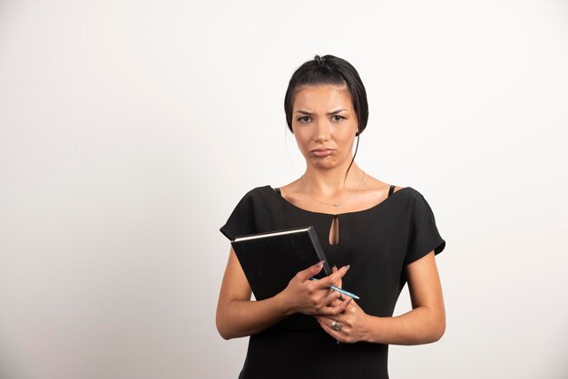 Free photo sad businesswoman posing with notebook on white wall.