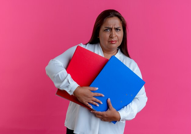 Sad casual caucasian middle-aged woman holding folders on pink