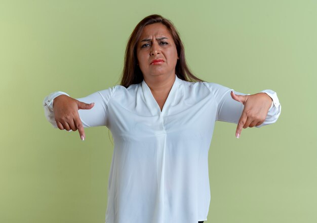 Sad casual caucasian middle-aged woman points at down isolated on olive green wall