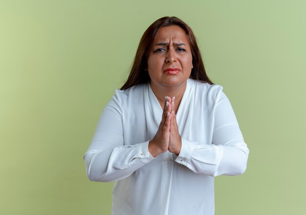 Грустная случайная кавказская женщина средних лет показывает жест молитвы, изолированную на оливково-зеленой стене