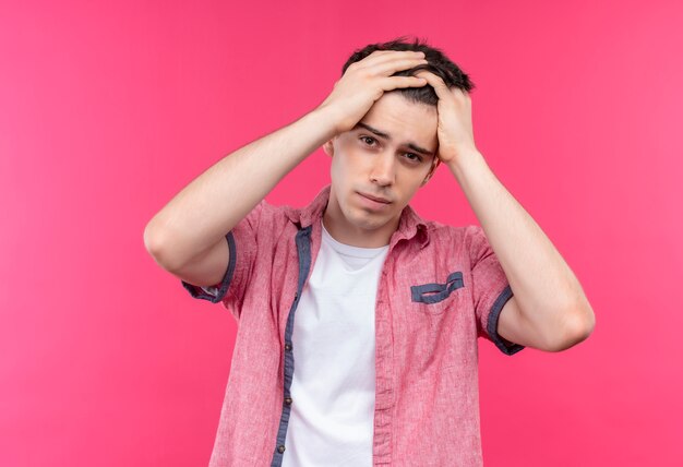 Foto gratuita il giovane ragazzo caucasico triste che porta la camicia rosa ha afferrato la testa su fondo rosa isolato