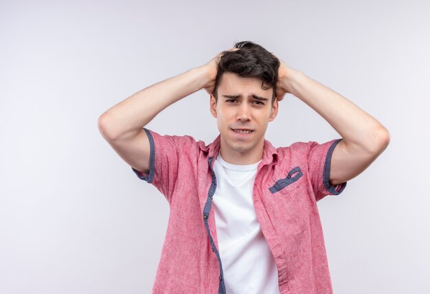 Sad caucasian young guy wearing pink shirt put his hands on head on isolated white background