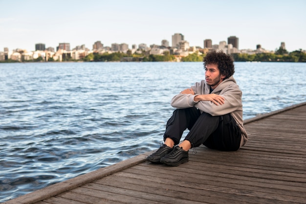 Free photo sad and contemplative man sitting by the lake