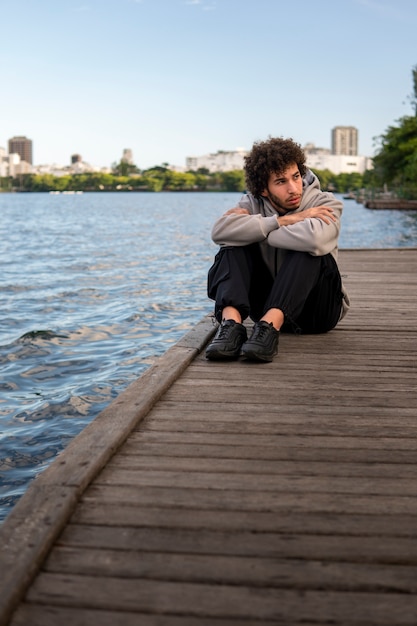 Foto gratuita uomo triste e contemplativo seduto in riva al lago