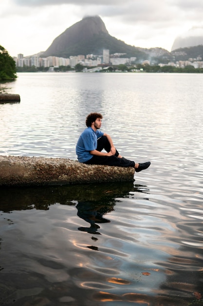 Foto gratuita uomo triste e contemplativo seduto in riva al lago