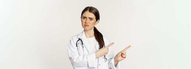 슬프고 실망한 여성 의사가 짜증스럽게 손가락질을 하고 서 있는 것에 불만을 품고 인상을 찌푸리고 있다