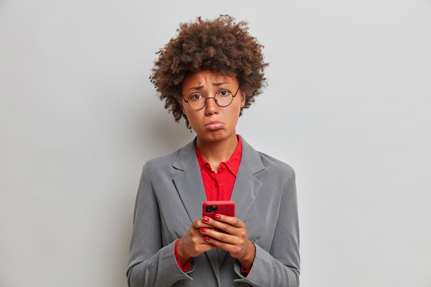 Печально разочарованная женщина-менеджер или исполнительный помощник имеет проблемы на работе, использует мобильный телефон, ждет важного звонка, не может решить сложную ситуацию, стоит в помещении. Технология