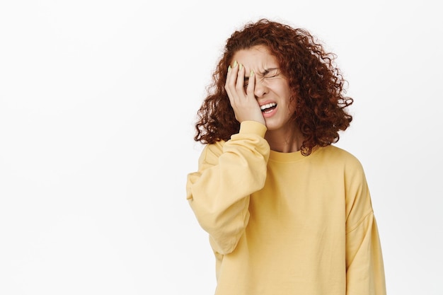 Sad and disappointed redhead woman facepalm, looking upset, disstressed by bad upsetting news, standing frustrated against white background