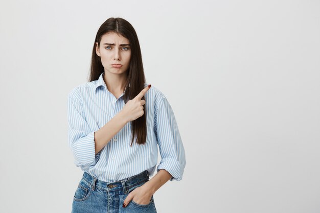 Sad disappointed woman pouting, pointing upper right corner with regret