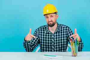 Free photo sad engineer is pointing down with forefingers on blue background