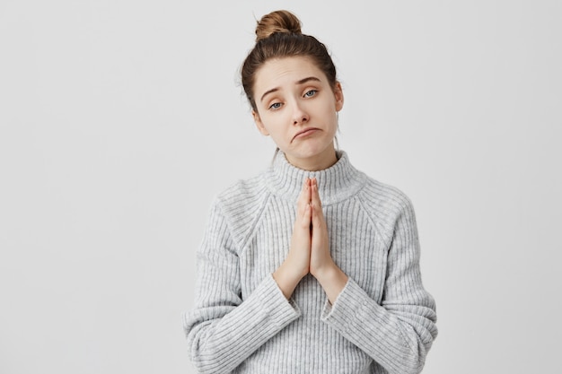 Sad facial expressions of pretty lady with hands together for supplication. Female youngster being trendy beseeching parents for money. Body language