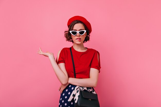 Sad female model in french attire posing. Pretty caucasian girl in red beret standing with upset face expression.