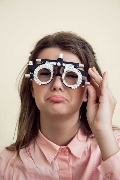 Грустная девушка имеет проблемы с глазами. Портрет расстроенной мрачной европейской женщины в кабинете офтальмолога, проверяющей зрение сидя и носящей фороптер, сожалеющей о том, что она испортила зрение возле компьютера