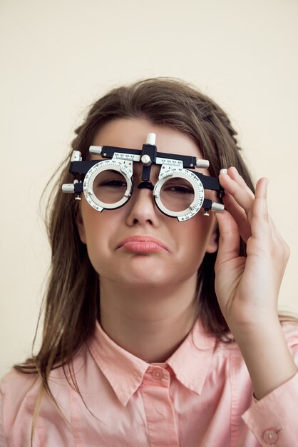 Sad girl has eye problems. Portrait of upset gloomy european woman in ophthalmologist office, testing vision while sitting and wearing phoropter, regretting that she spoilt sight near computer