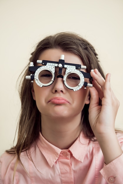 Sad girl has eye problems. Portrait of upset gloomy european woman in ophthalmologist office, testing vision while sitting and wearing phoropter, regretting that she spoilt sight near computer