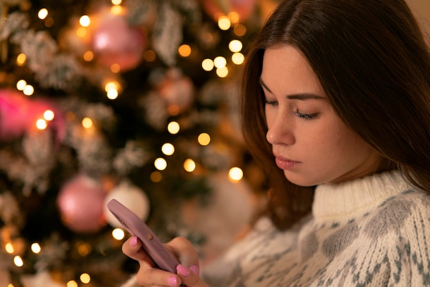 スマートな​お祝い​の​クリスマスツリー​の​女性​の​背景​に​携帯​電話​を​持っている​悲しい​女の子​...