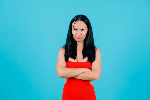 Sad girl is looking at camera by crossing arms on blue background