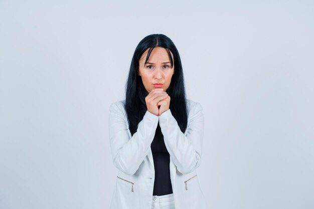 Sad girl is looking at camera by holding hands together on chin on white background