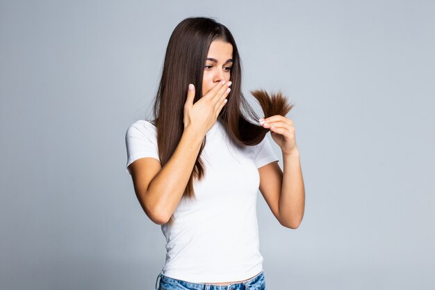 Sad girl looking at her damaged hair isolated on white