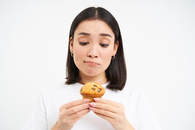 無料写真 悲しい女の子は、ダイエットの白い背景にカロリーが多すぎるおいしいカップケーキを見ています