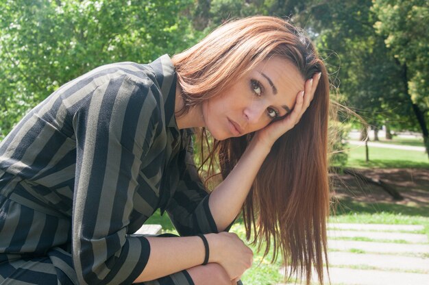 Sad girl sitting on bench in park