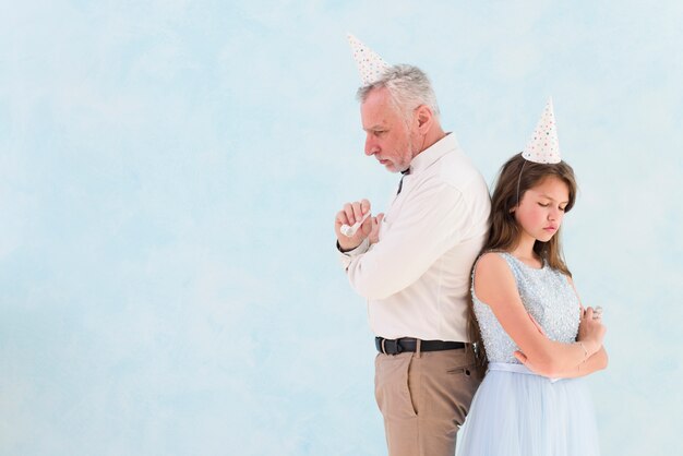 Sad girl standing behind her grandfather against blue background