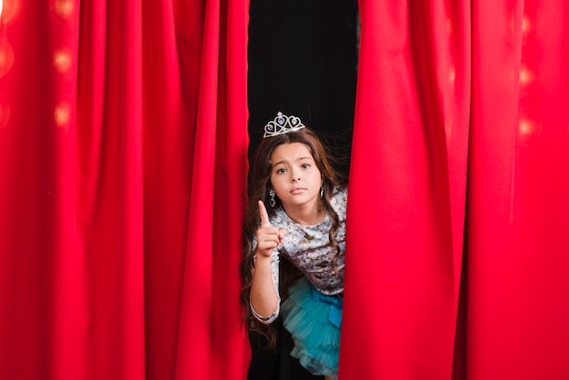 Sad girl standing behind the red curtain gesturing